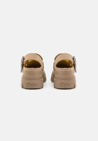 Pantofi cu platformă bej, din suede, cu curea ajustabilă și talpă din cauciuc texturat. Prezintă inscripția "Buffalo" embosată pe călcâi.