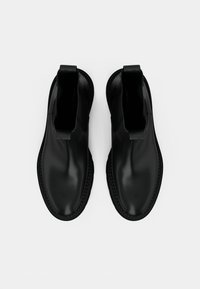Svarta vattentäta anklar stövlar med en slät, glansig yta. Elastiska sidor och texturerade gummisulor för bra grepp. Minimalistisk design utan synlig hårdvara.