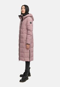 Lang, pink puffer Jakke med hætte, med lynlåslukning, sidelommer og quiltet design. Bæres med sorte bukser og støvler.