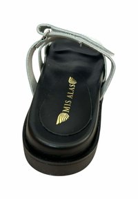 Sandal de plataforma negra con una correa plateada, que presenta una suela curva y un logo dorado grabado en la plantilla negra. Textura de cuero suave.