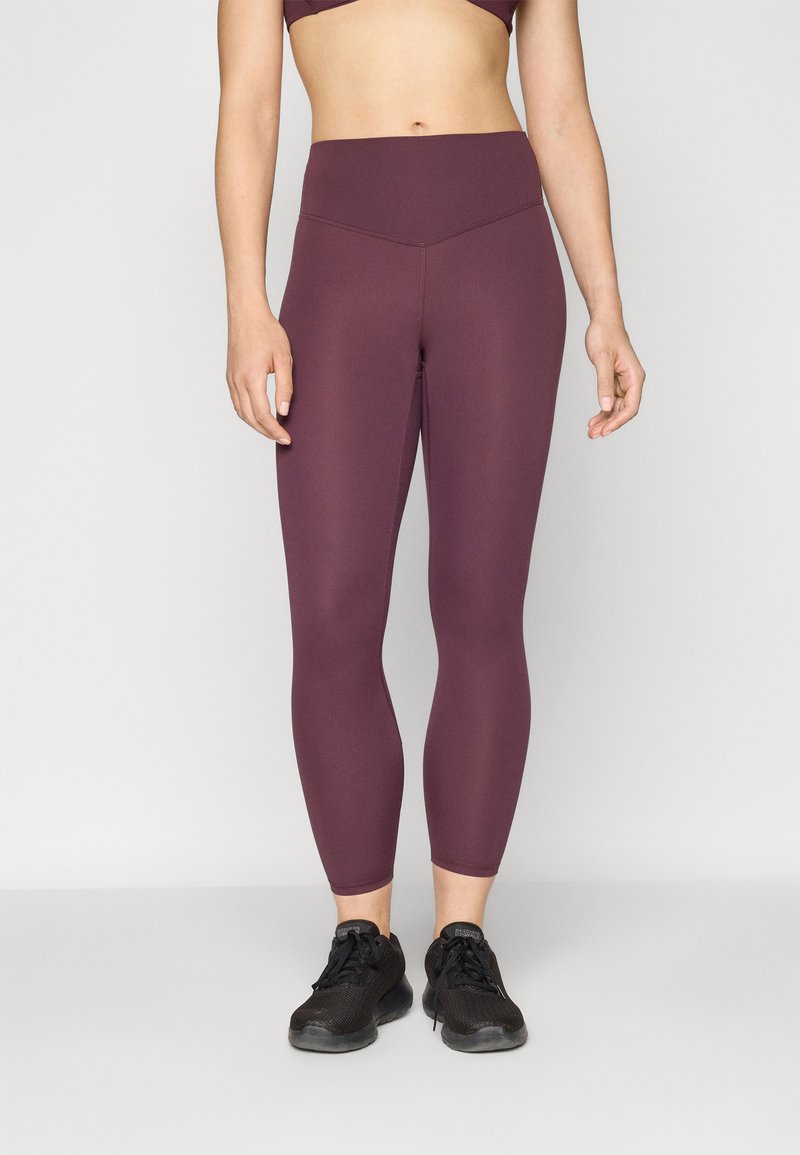 Leggings bordeaux a vita alta con una texture liscia e un design aderente. Abbinati a scarpe da ginnastica nere per un look sportivo.