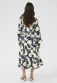 Cvečna maxi obleka v morsko modri in kremni barvi, narejena iz lahkega blaga. Ima dolge rokave, gubano pasnico in plasten gladek rob. Vključene so ravne sandale.