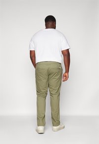 Pantalones de algodón en verde oliva, ajustados en la parte inferior, con bolsillos traseros, combinados con una camiseta blanca básica y zapatillas beige.