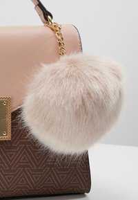 Beżowa i brązowa torebka z złotym zapięciem i łańcuszkiem, z dużym puszystym różowym futrzanym brelokiem jako akcesorium.