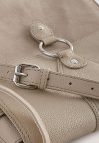 Geantă de mână din piele bej cu suprafață texturată, prevăzută cu o cataramă și un inel argintii, accente cusute și o curea netedă.