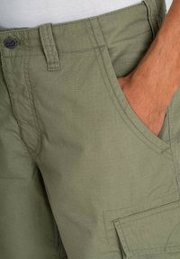 Pantalones cortos cargo verdes hechos de un tejido ligero, que presentan un patrón de cuadrícula texturizada, bolsillos laterales y un cierre de botón en la cintura.