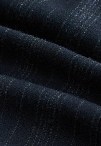 Sötét tengerészkék gyapjú anyag, finom függőleges csíkokkal. A felülete puha, enyhén bolyhos, színárnyalatokban változatos.