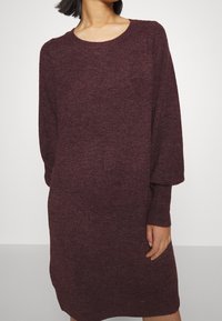 Robe pull en maille bordeaux avec un col rond, des manches longues et une coupe décontractée. Tissu texturé et poignets côtelés, longueur mi-cuisse.