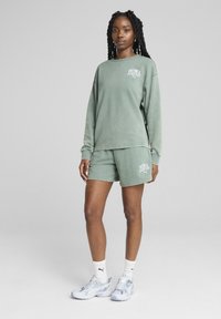 Sweat-shirt en coton vert avec logo PUMA et shorts assortis. Le sweat-shirt a des manches longues ; les shorts sont au-dessus du genou avec une coupe décontractée.