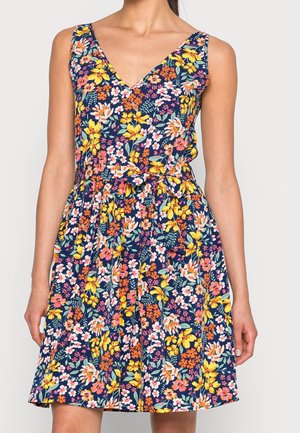Mouwloze jurk met V-hals, marineblauwe achtergrond en een fleurig bloemenpatroon in geel, roze, oranje en wit, met een strikceintuur in de taille.