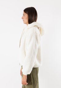 Weißer Fleece-Hoodie mit strukturiertem Obermaterial, lässiger Passform und Kapuze mit Zugband, kombiniert mit grünen Cordhosen.