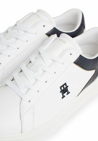 Białe skórzane sneakersy z czarnym akcentem na pięcie, tonowane sznurowadła, teksturowana powierzchnia i czarne logo z boku.