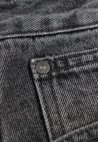 Czarny i szary denim z teksturowanym wzorem, z metalowym guzikiem i widocznymi detalami przeszycia na obszarze kieszeni.