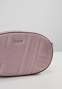 Pink leather bag with quilted pattern, featuring embossed "DKNY" logo and contrasting stitching. Rounded shape and smooth texture visible.