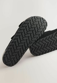 Mustad mustreeritud mustad jalanõude tallad, millel on kalasaba muster; kanna kohapealt kerge kumerus ja erinev paksus, et tagada parem haarduvus ja tugi.