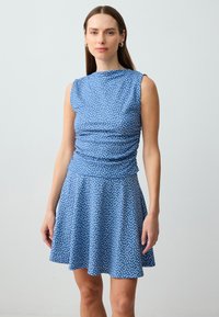 Blauwe mouwloze jurk met een geplooide bovenkant en uitlopende rok, voorzien van een witte stippenpatroon en gladde, lichte stof.