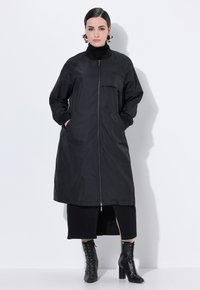 Chaqueta negra larga con cierre de cremallera, puños acanalados y bolsillos laterales. Tela texturizada con un diseño minimalista y un solo bolsillo frontal.