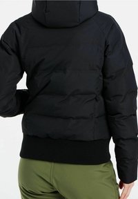 Personne portant une doudoune noire avec ourlet côtelé et capuche, associée à un pantalon vert olive, vue de dos.