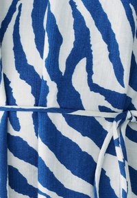 Tkanina s plavim i bijelim uzorkom zebre, s teksturiranom površinom i detaljem vezanog pojasa u struku, ističući izražen uzorak i kontrast boja.