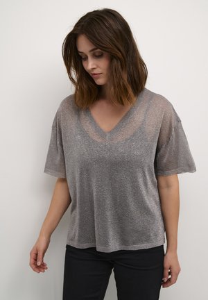 Haut argenté à manches courtes en V avec coupe loose, tissu transparent et texture lisse. Associé à un pantalon noir.