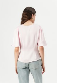 Blusa corta de manga corta en rosa claro con escote redondo. Tejido suave con un ligero brillo, mangas globo suaves y cuerpo entallado. Estilo casual.