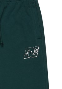 Dunkelgrüne Sweatpants mit elastischem Taillenbund, Seitentaschen und einem weißen DC-Logo mit einem Stern, das auf dem linken Bein aufgedruckt ist.