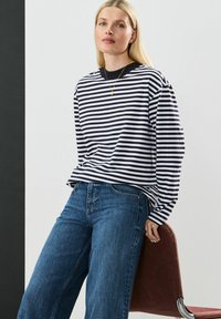 Langærmet striped skjorte i sort og hvid, parret med blå denimjeans. Skjorten har en rund hals og afslappet pasform.