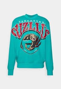 Sudadera turquesa con un gráfico redondo que presenta un oso, texto 'Vancouver Grizzlies' y acentos rojos. Cuenta con puños y cuello de canalé.