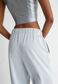 Top corto grigio e pantaloni jogger azzurri chiari con finitura texturizzata. I pantaloni jogger presentano una vita elasticizzata e tasche laterali. Accento del logo dorato visibile.