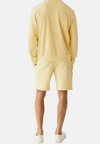 Felpa gialla in cotone con vestibilità comoda, maniche raglan e pantaloni corti abbinati. Sneakers bianche completano l'outfit casual.
