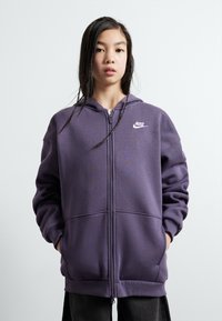 Ljubičasti dukserica sa zipped zatvaranjem, izrađena od mekanog materijala, s prednjim patentnim zatvaračem, dva džepa i malim bijelim Nike logom na prsima.