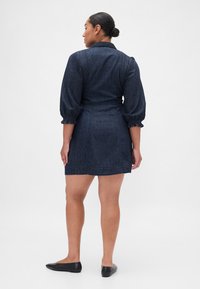 Rochie din denim cu nuanță albastru închis, mâneci bufante și talie strâmtă, cu design tip cămașă și lungime deasupra genunchiului.