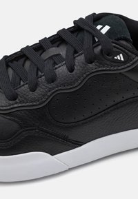 Črne teniske z zgornjim delom iz teksturirane usnje, zaobljenim nosom, toniranimi vezalkami, perforiranimi stranicami in belim gumijastim podplatom. Dodatki vključujejo detajle logotipa.