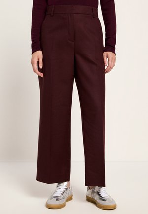 Burgundy wide-leg trousers with a smooth texture, tailored fit, and side pockets. Paired with metallic silver sneakers for a contrasting look.