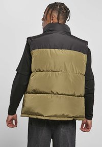 Polstret vest med høj krave, der har en sort øverste sektion og en olivengrøn nederste sektion. Glat tekstur, synlig syning og lagdelt design.