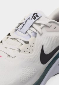 Λευκό αθλητικό παπούτσι Nike με μαύρο σήμα swoosh, λευκά κορδόνια και υφασμάτινη θηλιά με την ένδειξη "RUN Structure 26" στη γλώσσα.