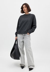 Zwarte sweatshirt met een ronde hals, relaxed fit en geribbelde manchetten, gecombineerd met lichtgrijze wijde jeans en een grote zwarte tote bag.