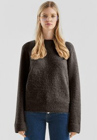 Ciemnoszary, teksturowany sweter o luźnym kroju, z szerokimi rękawami i okrągłym dekoltem, w zestawieniu z niebieskimi dżinsami. Miękka, przytulna tkanina.