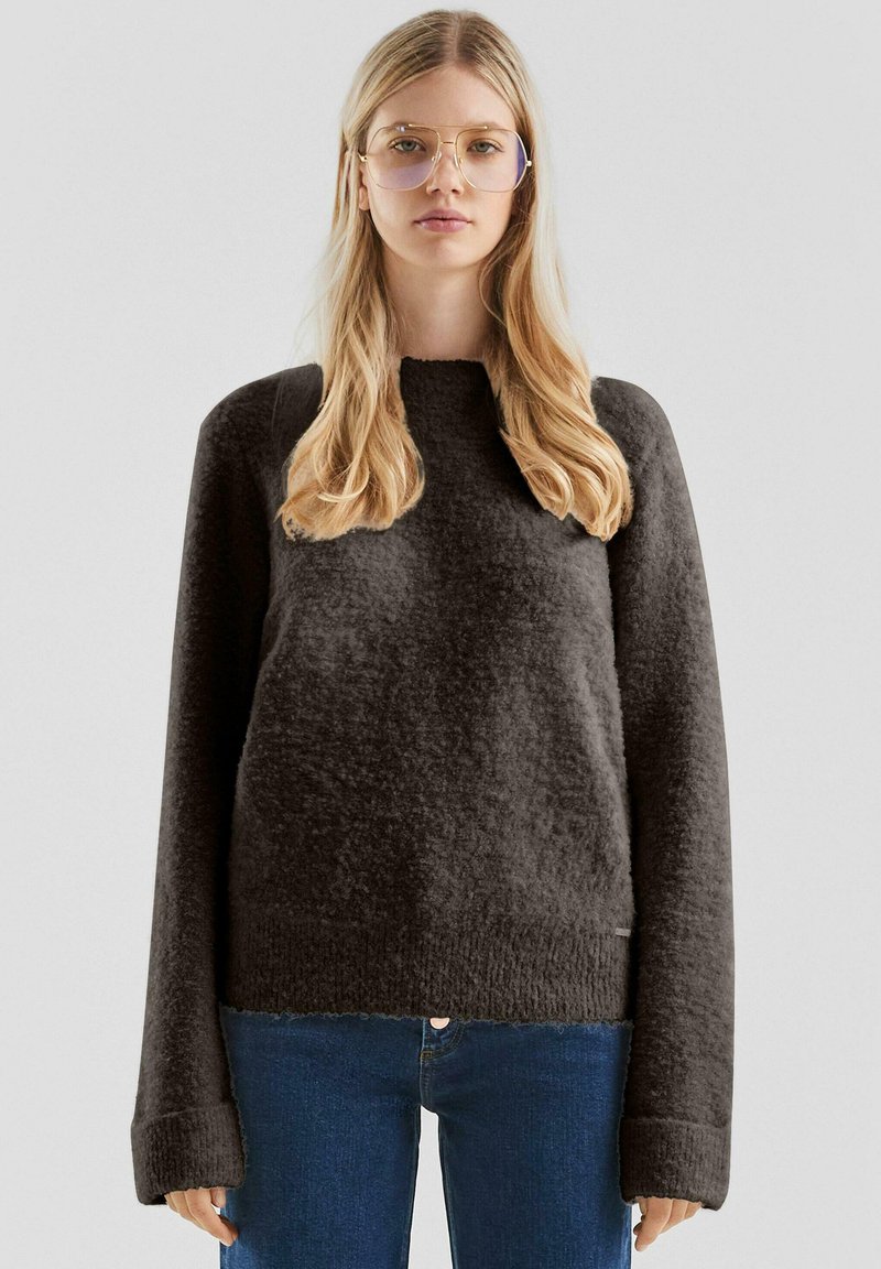 Ciemnoszary, teksturowany sweter o luźnym kroju, z szerokimi rękawami i okrągłym dekoltem, w zestawieniu z niebieskimi dżinsami. Miękka, przytulna tkanina.