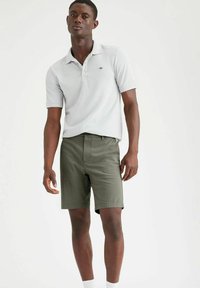 Polo shirt grigio chiaro con maniche corte e colletto, abbinato a pantaloni corti verde oliva. I pantaloni hanno una finitura strutturata e un taglio pulito.