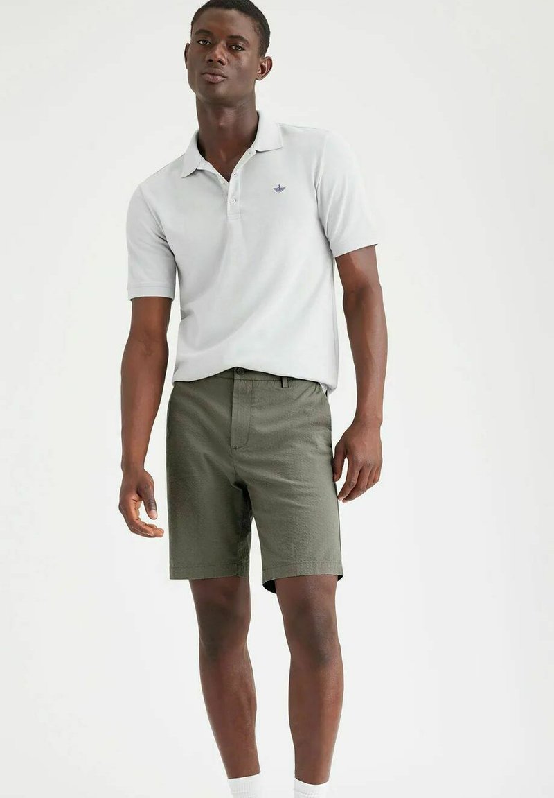 Polo shirt grigio chiaro con maniche corte e colletto, abbinato a pantaloni corti verde oliva. I pantaloni hanno una finitura strutturata e un taglio pulito.