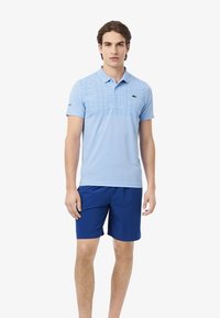 Polo bleu clair avec un motif texturé en grille sur la poitrine, associé à un short bleu foncé. Tissu en mélange de coton.