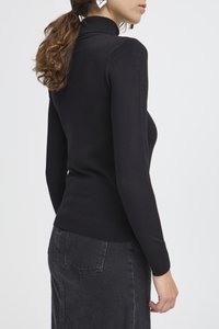 Pull noir à col roulé à manches longues avec une coupe ajustée, des poignets et un ourlet côtelés. Porté avec une jupe en jean grise, vu de dos.