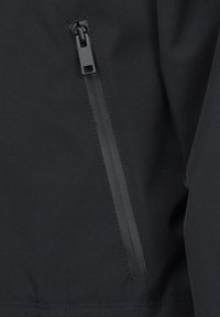 Schwarze Jacke mit einem Reißverschlusstasche auf der linken Seite. Das Material wirkt strukturiert und wetterbeständig mit sauberen Nähten.