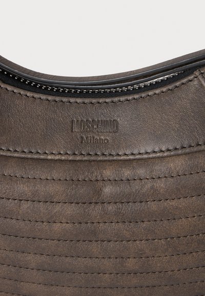 Κοντινή λήψη καφέ δερμάτινης τσάντας Moschino Milano που δείχνει φερμουάρ και υφασμένη λεπτομέρεια ραφής.