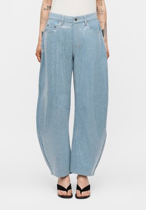 Lyseblå viddebukser med subtile palietdetaljer ved taljen, båret med sorte åben-toe sandaler og en hvid top.