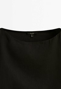 Blouse noire à col rond avec une texture lisse et une petite étiquette de marque à l'encolure indiquant la taille.