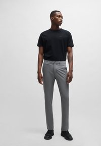 Černé tričko s krátkým rukávem a logem; světle šedé slim-fit kalhoty; hladká látka; černé tenisky; model stojí před jednobarevným pozadím.