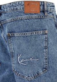 Blue denim jeans with a brown leather patch. The back pocket features white embroidered text "Kani." Includes visible stitching details.