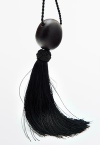 Portachiavi con nappina nera che presenta una perlina rotonda in legno scuro, attaccata con un cordino intrecciato, che si estende in lunghi filamenti texturizzati.